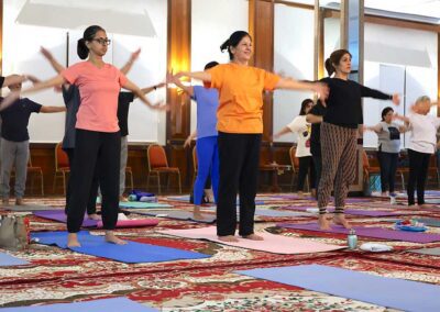 Participants in Miracle Yoga class at Gandhi Seva Loka Jakarta standing on mats and performing coordinated arm exercises during the Wednesday class.