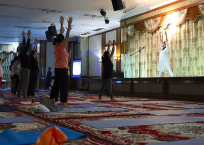 Participants raising arms while following the instructor’s guidance on stage during Miracle Yoga class at Gandhi Seva Loka in Jakarta.