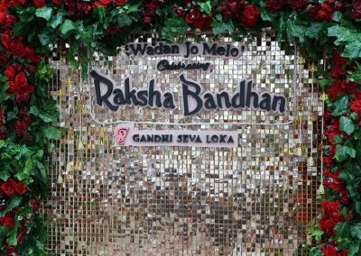 Glittering backdrop for Raksha Bandhan celebration by Gandhi Seva Loka in Jakarta, framed with red roses and green leaves.