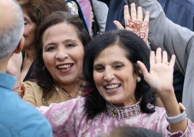 Two smiling women enjoying the Raksha Bandhan festivities at Gandhi Seva Loka, waving and celebrating in a joyful crowd.