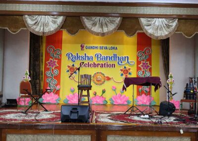 Colorful stage decorated with floral artwork and lotus designs for Raksha Bandhan celebration at Gandhi Seva Loka